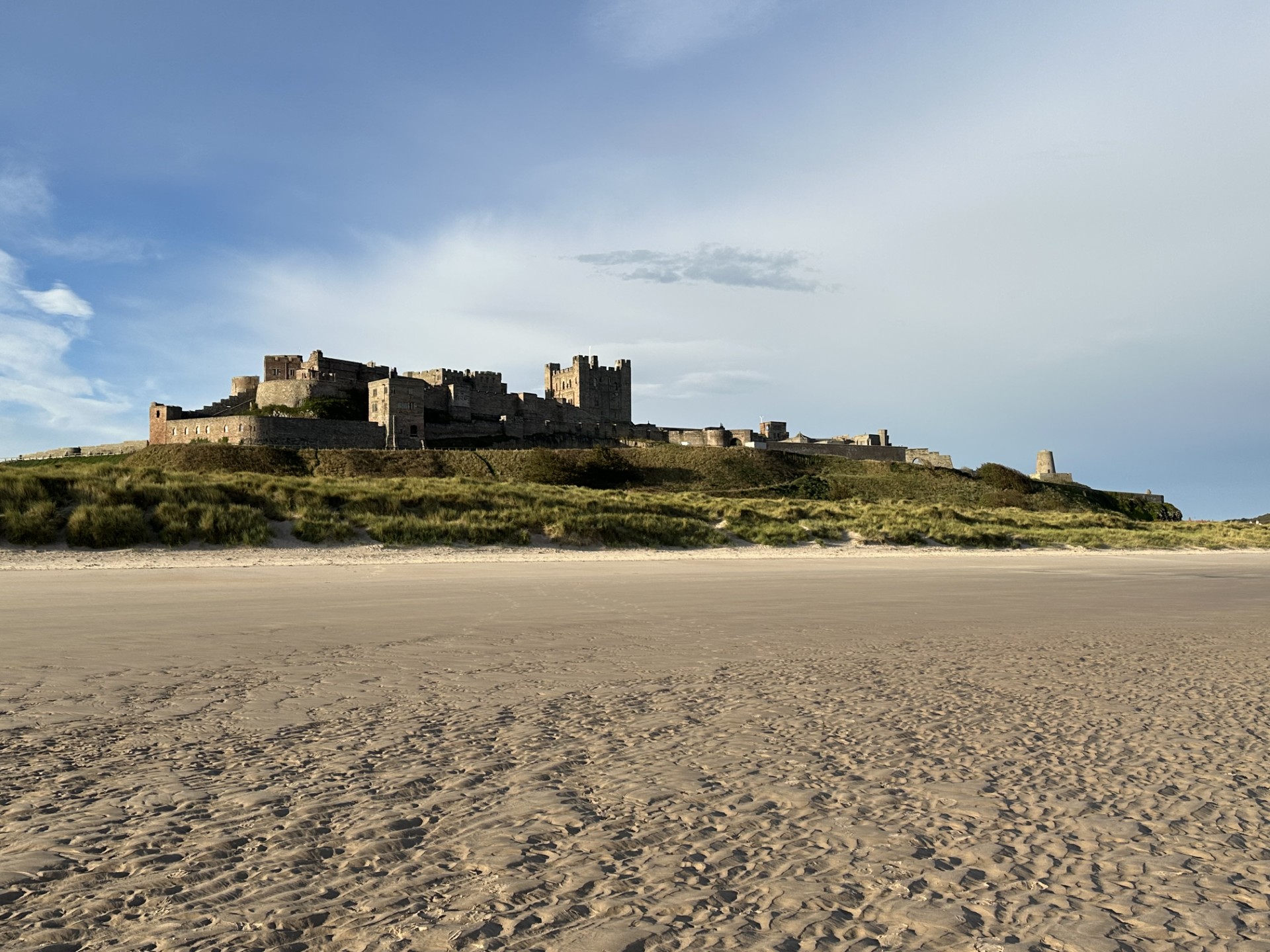 A large stone castle sits slightly raised above a wide sandy beach.