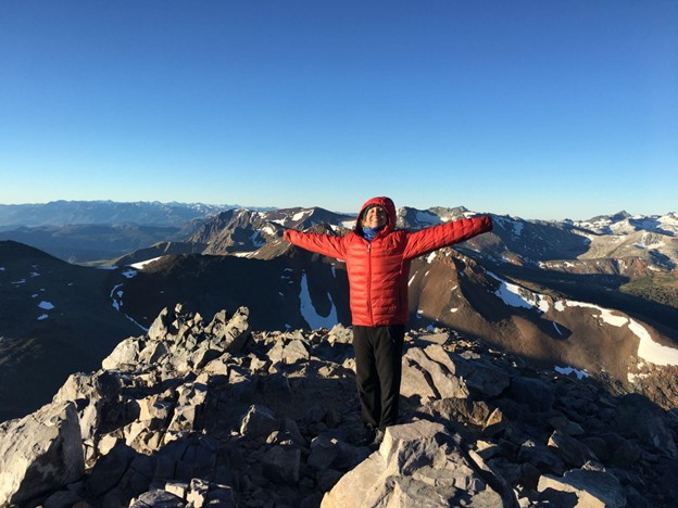 student standing on top of a mountain with her arms outstretched and a big smile on her face