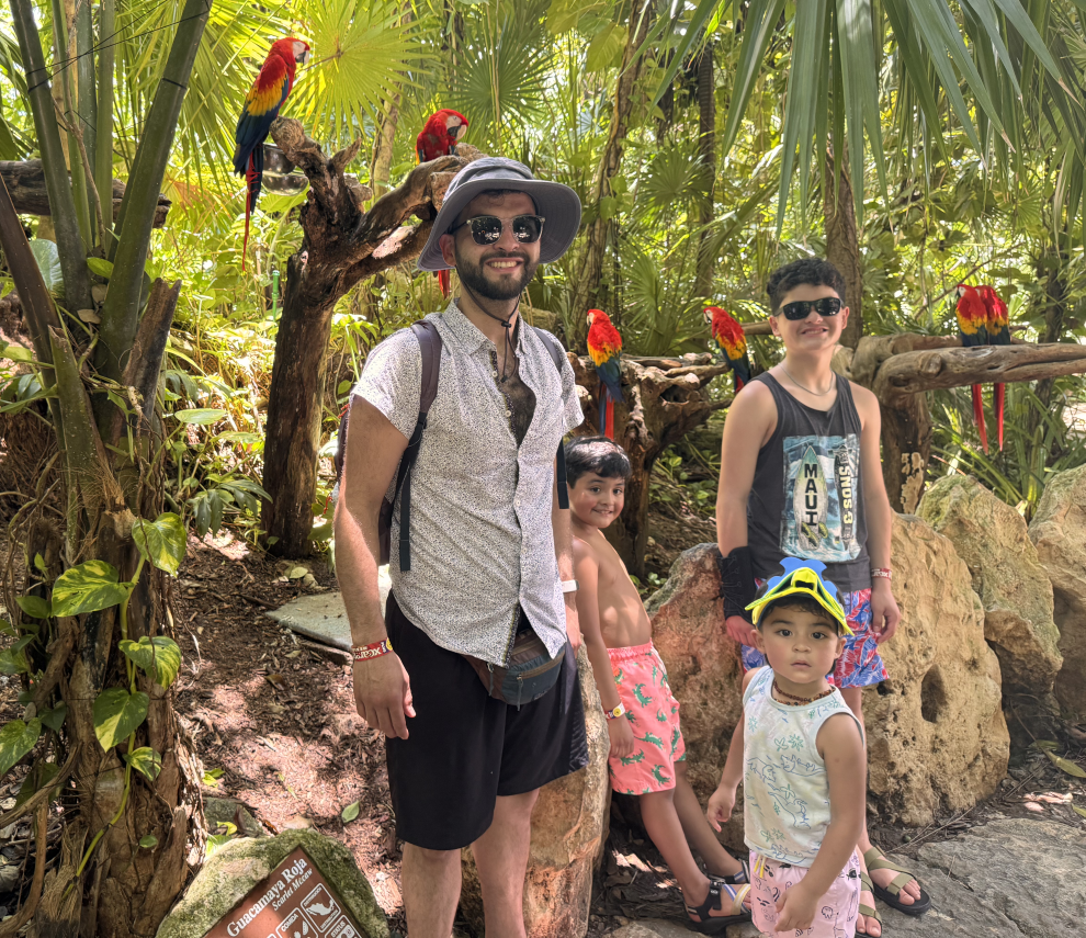Manuel De La Garza standing with his sons Luca, Mika and Levi surrounded by red parrots
