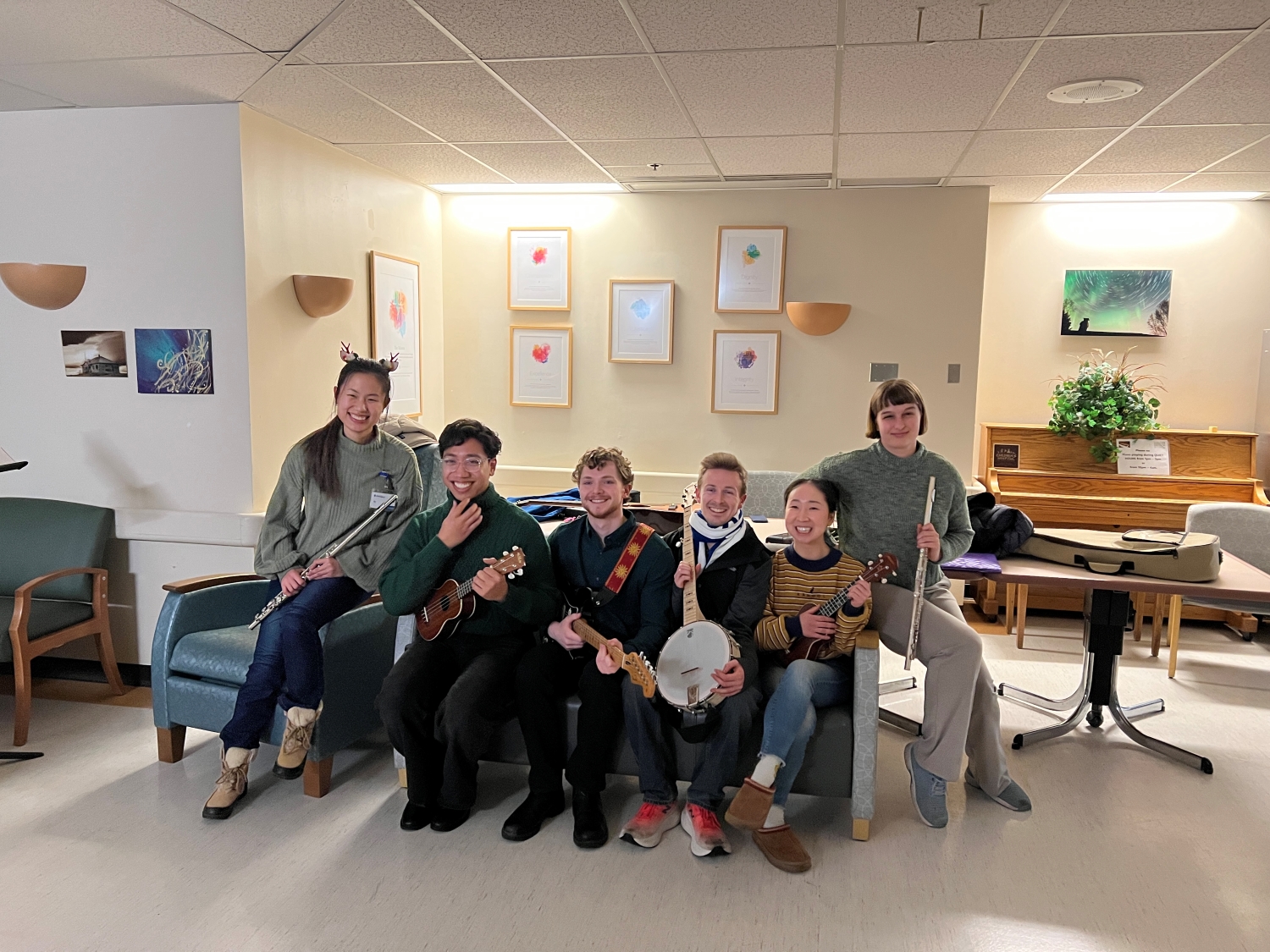 Six students dressed in festive outfits pose together with instruments in the hospital lobby