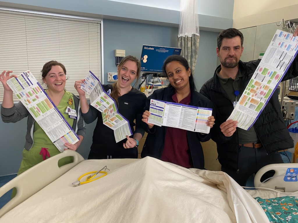 Four medical residents pose in front of an empty hospital bed with colorful charts