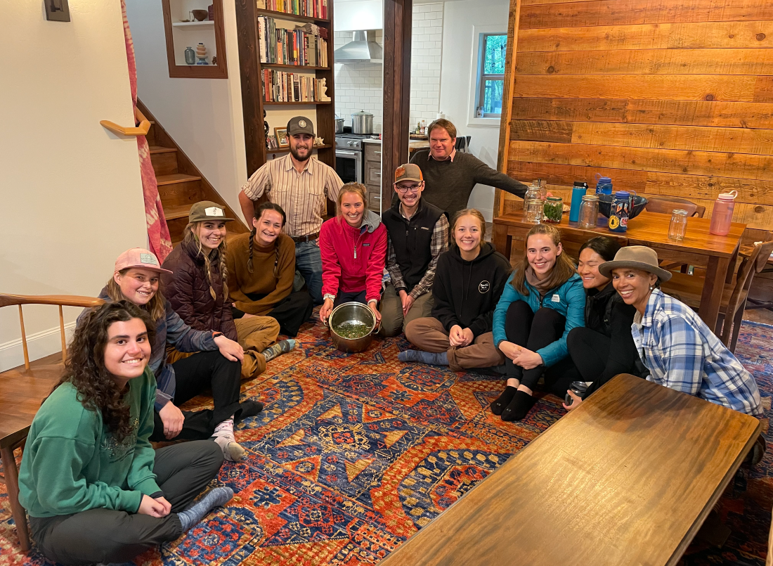 Students and Dr. Kirchhoff pose together in a large circle sitting on the floor of Pony Creek Homestead