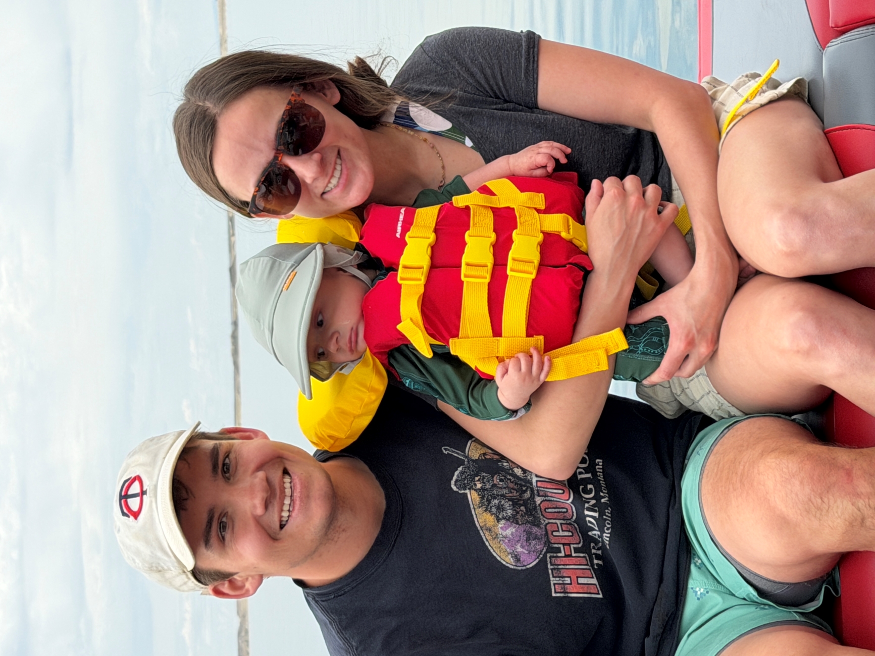 Ben Held poses with his wife and son in front of a body of water. Baby Winston is wearing a life jacket. 