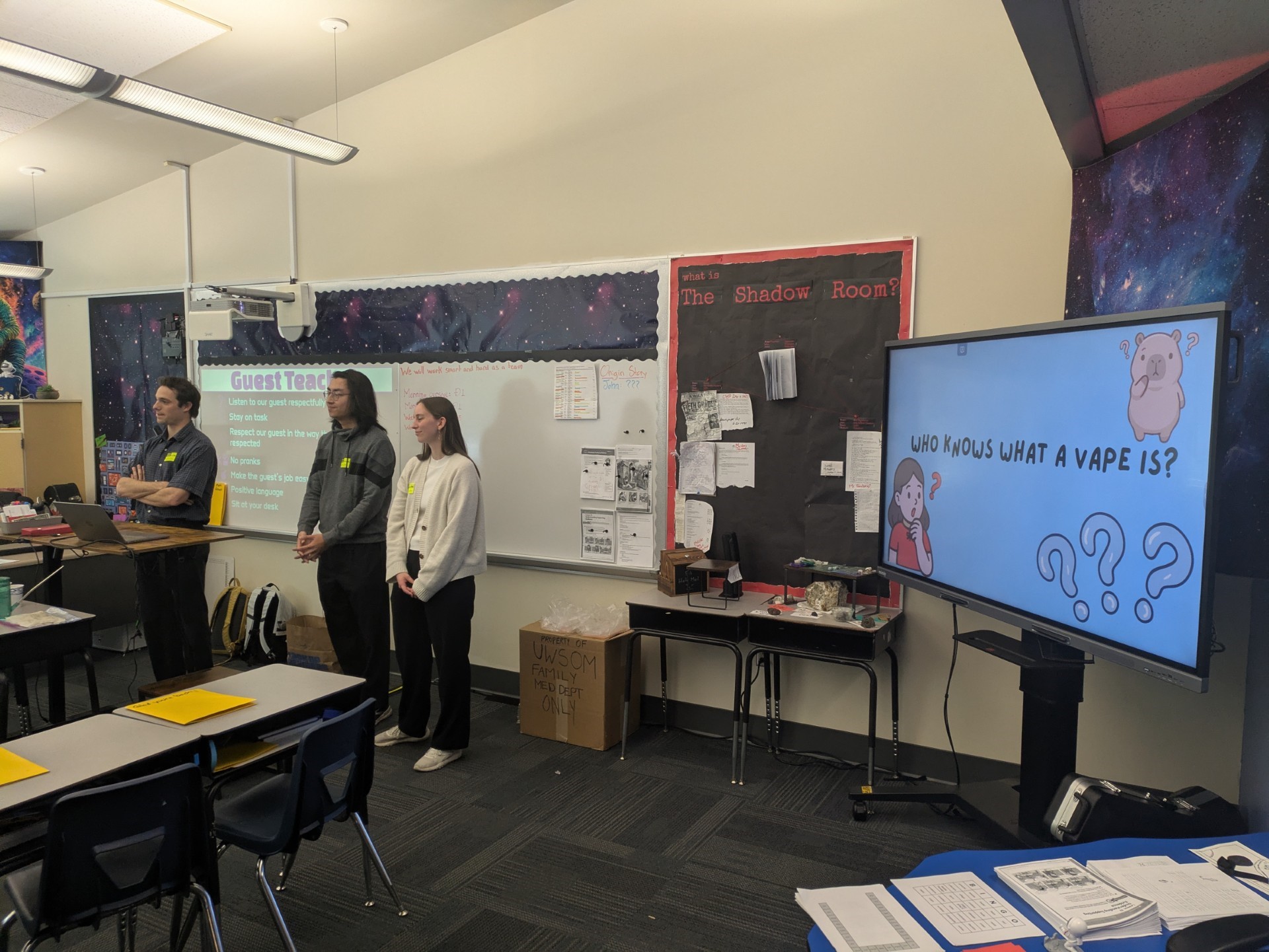 Three medical students stand in front of a digital screen as they present to a class of fifth graders about vaping prevention
