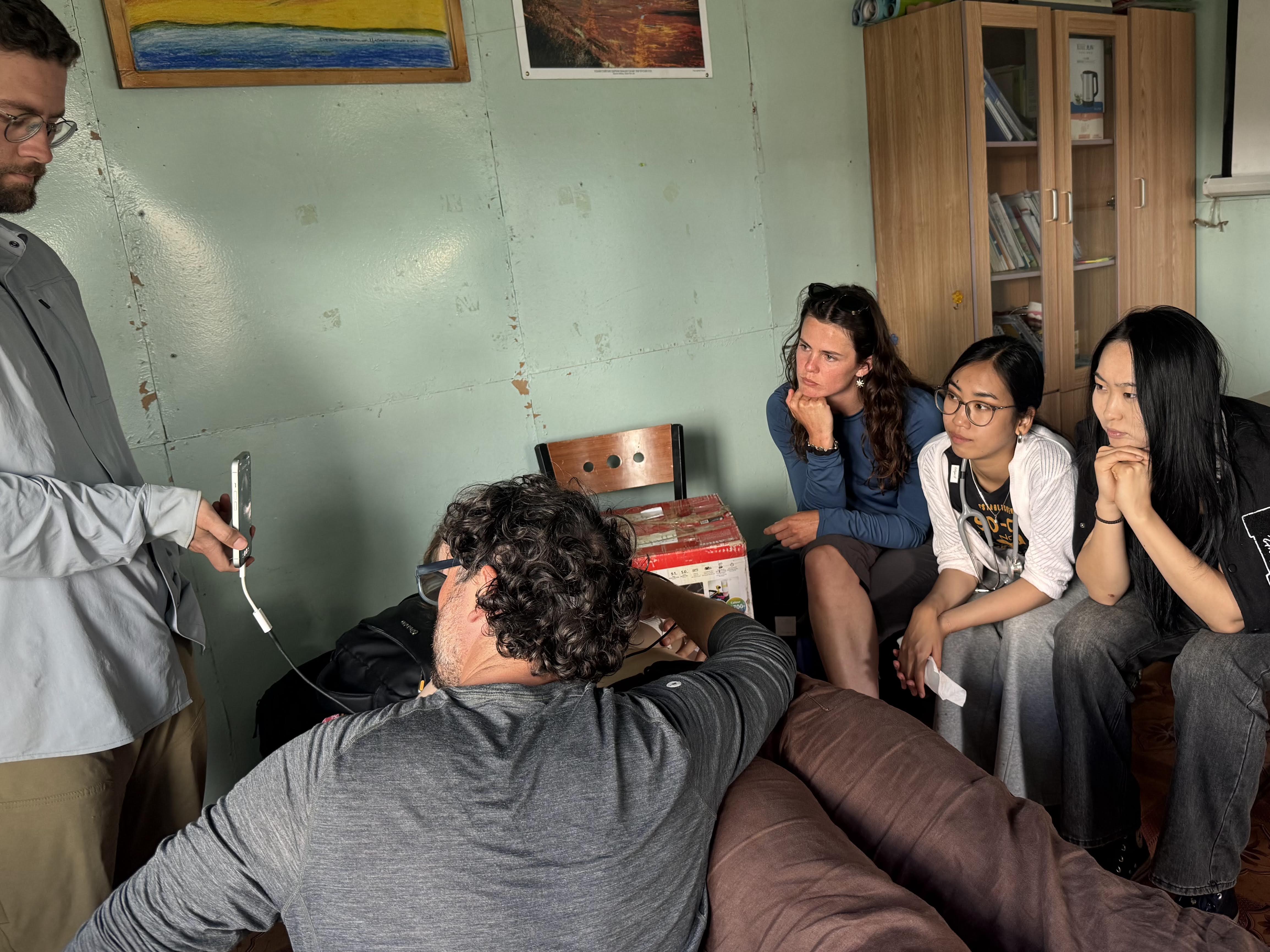 5 people sit in a room with green walls lined by benches