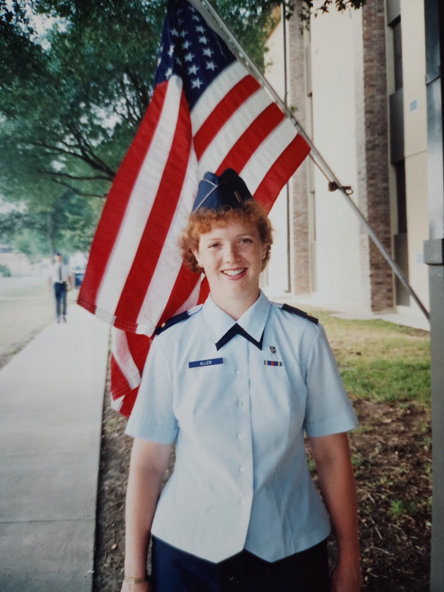 A young Suzanne Allen in her air force uniform poses in front of the American flag