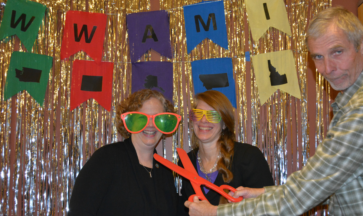 Suzanne poses in big costume glasses in front of a colorful WWAMI banner